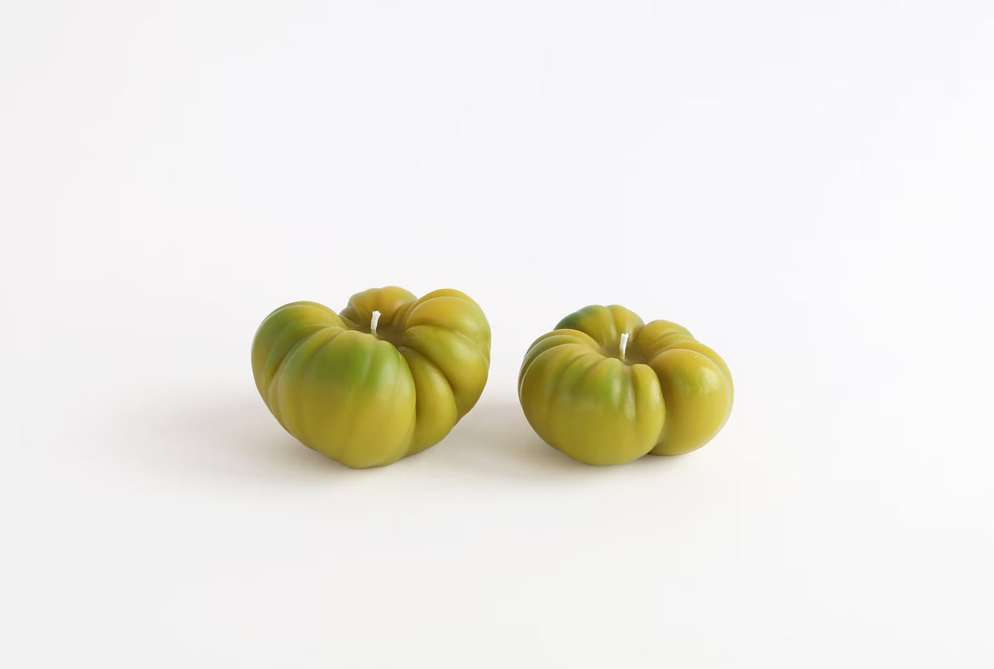 Two green tomatoes beeswax candles on a white background