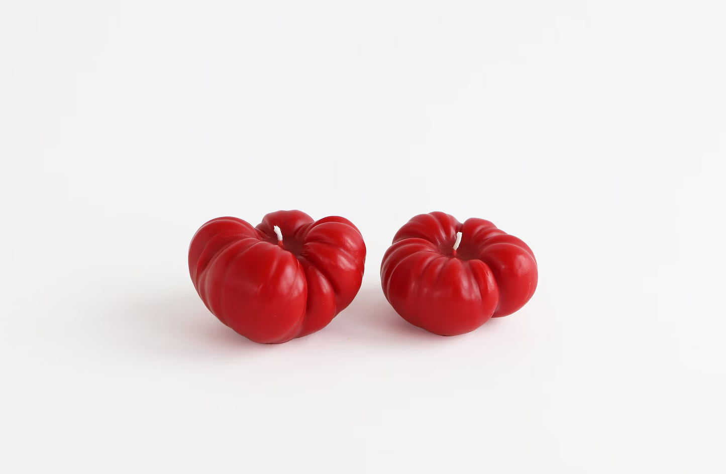 Two red tomatoes beeswax candles on a white background