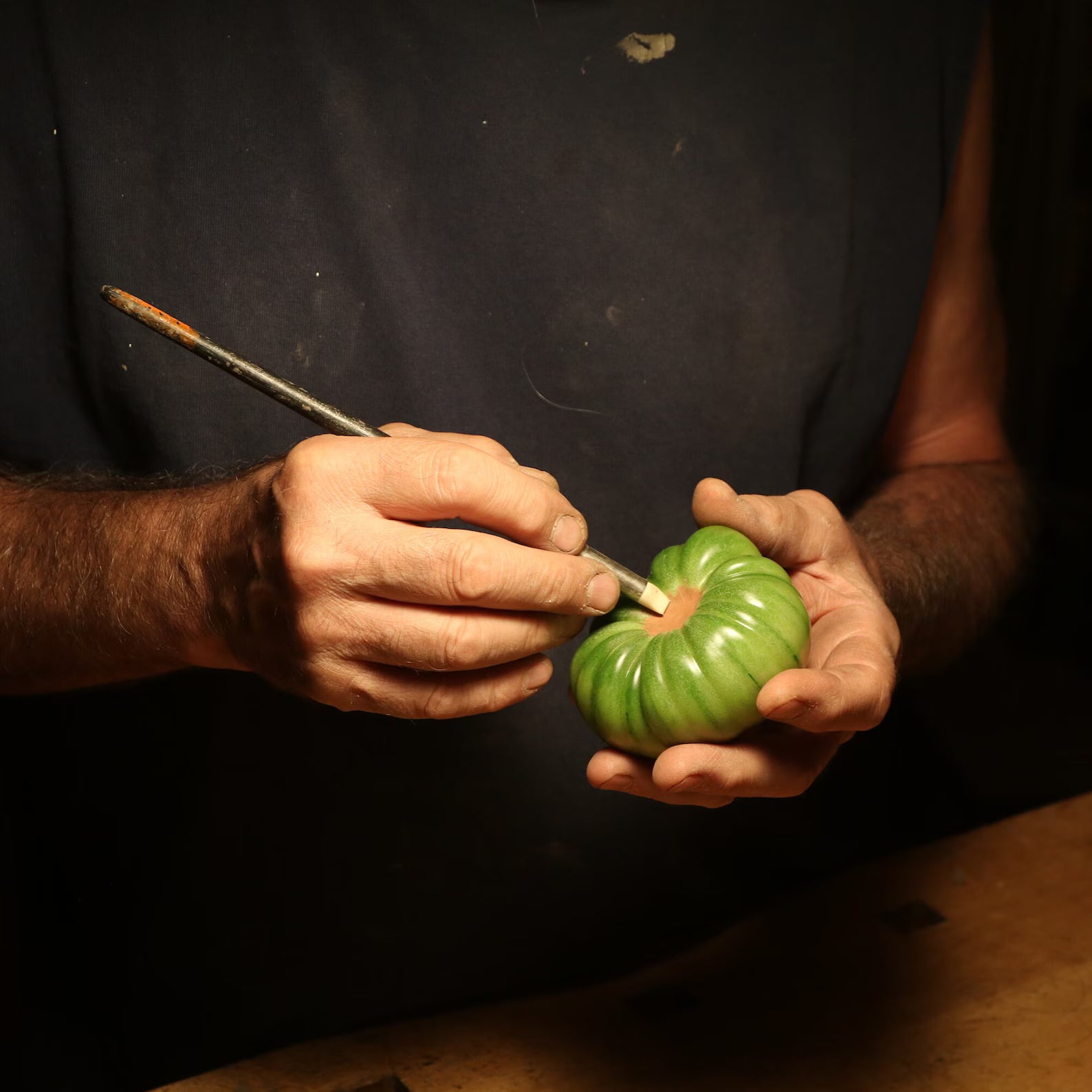 An artisanal green tomato beeswax candle in the making: in the hand of the mold maker holding a tool