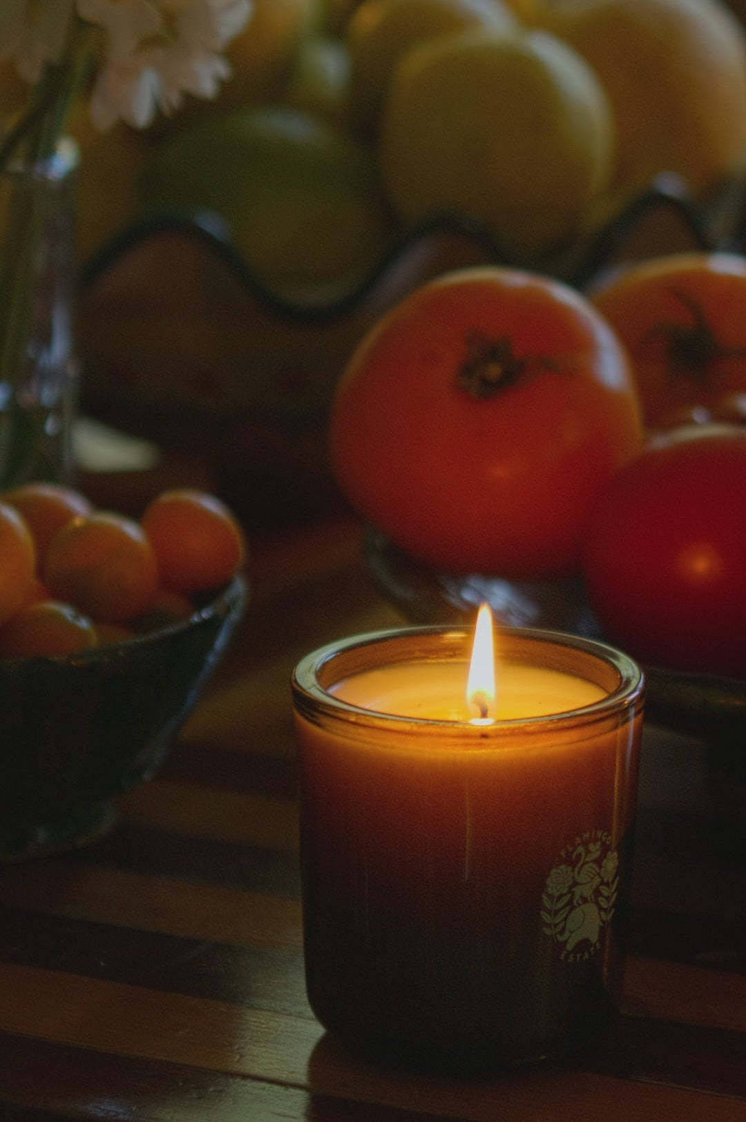 Flamingo Estate Candle with a fruit and flower arrangement in the background