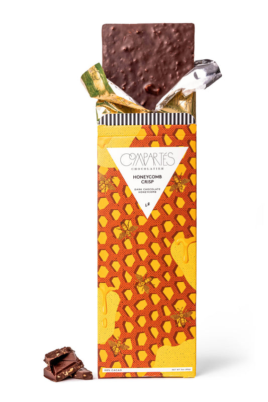 A crunchy honey dark chocolate bar from Compartes chocolate wrapped in a colorful packaging, yellow and orange.