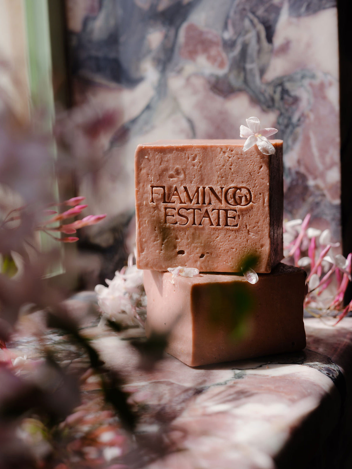 Jasmine & Rose square bar of soap with 'Flamingo Estate' branding on a stand with a floral background. 