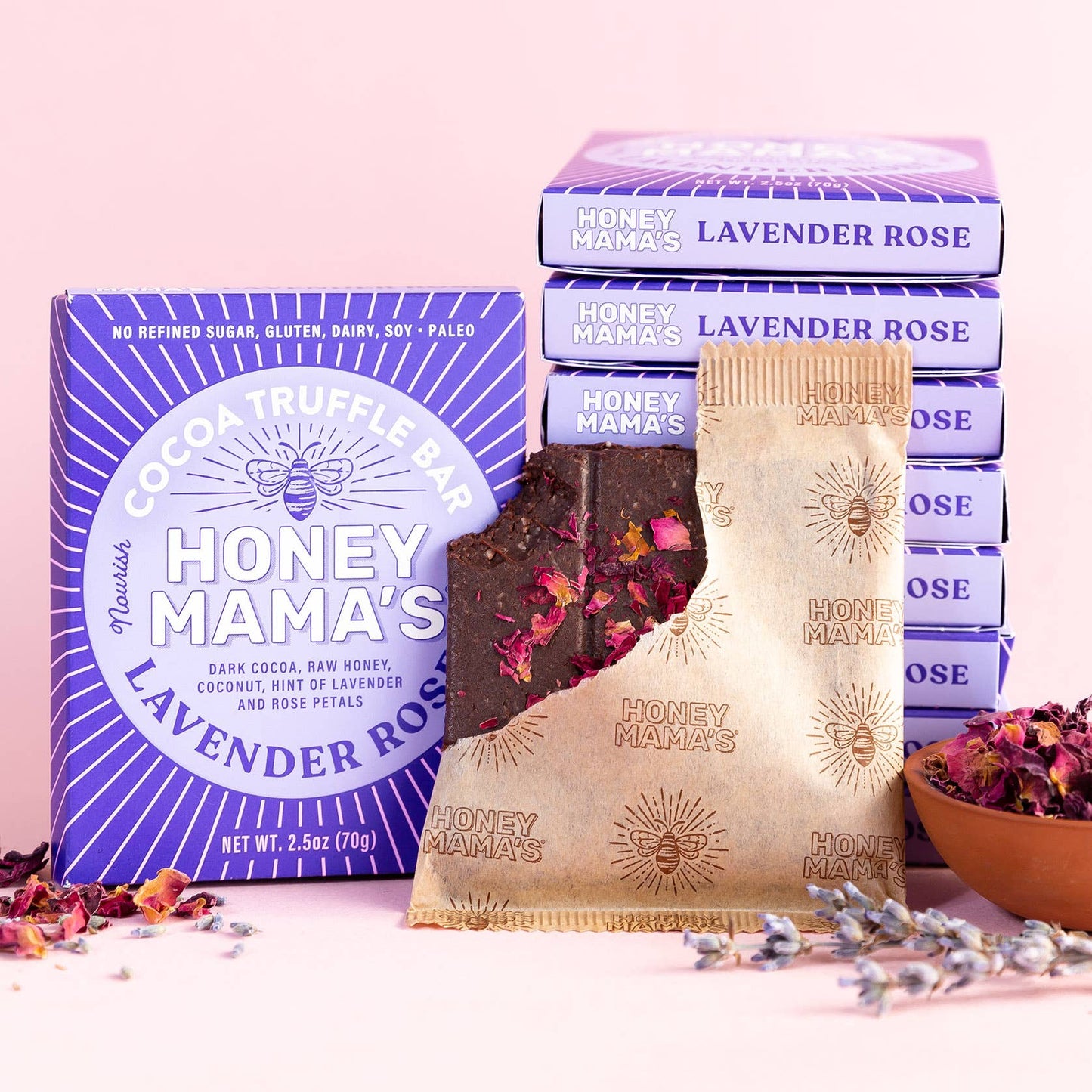 Multiple boxes of Honey Mama's Lavender Rose Cocoa Truffle Bar with one product visible, topped with red rose petals. On the packaging we can see that the bar is made from real foods only, paleo, refined sugar-free, dairy-free, and gluten-free.