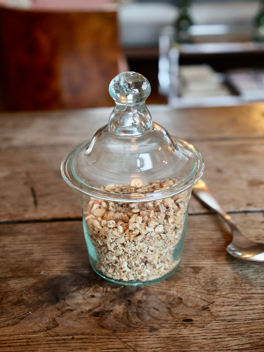 Glass jar with an elegant lid filled with small bits of nuts on a wooden surface