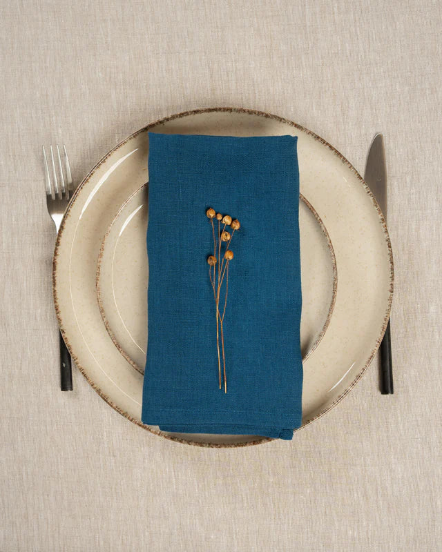 Cobalt blue linen napkin with dried flowers on a plate with cutlery on a beige tablecloth.