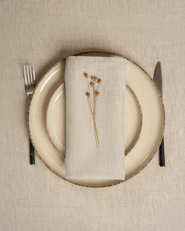 Set table with beige plate, natural beige linen napkin, and cutlery on a beige tablecloth.