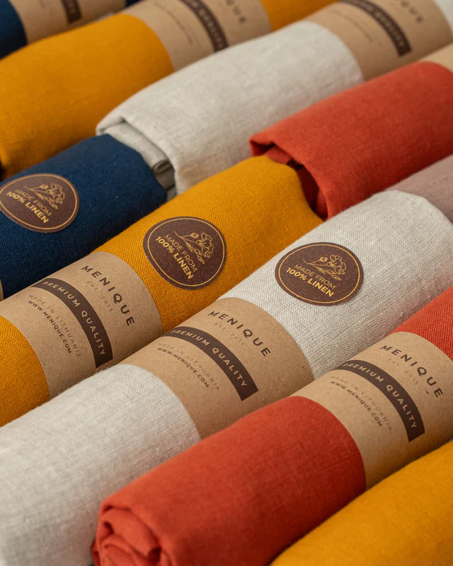 Rolled-up linen table runners with Menique labels in various colors.