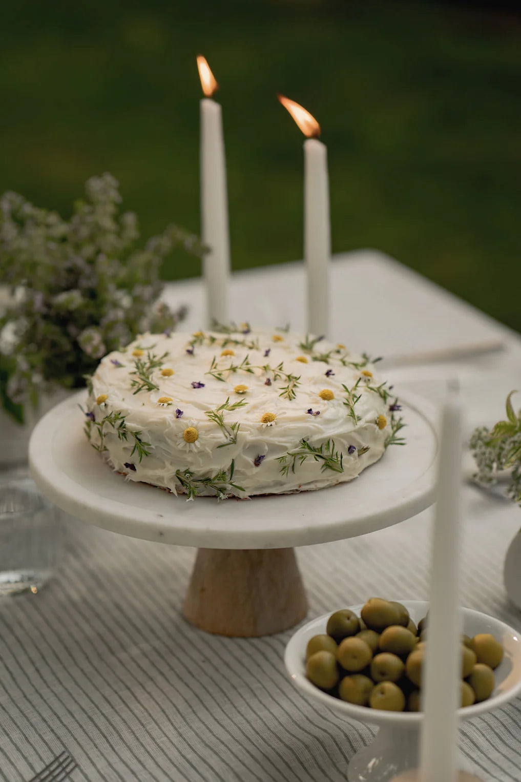 Decorative cake with candles on a white plate outdoors, on a green stripe linen tablecloth 