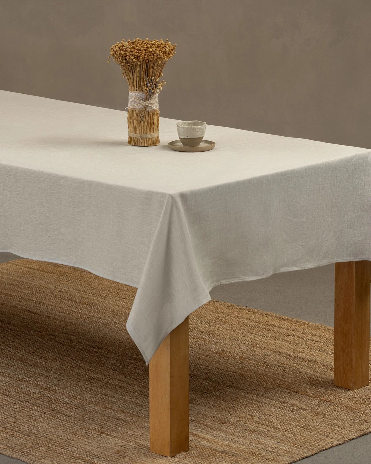 Natural beige tablecloth on a wooden table with a small decorative arrangement.