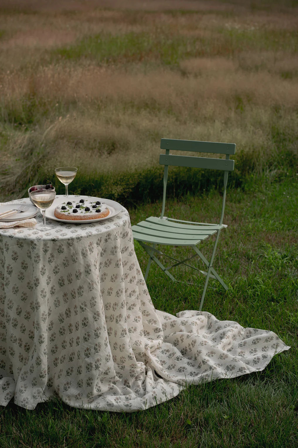 Outdoor setting with a floral linen tablecloth-covered table and chair in a field