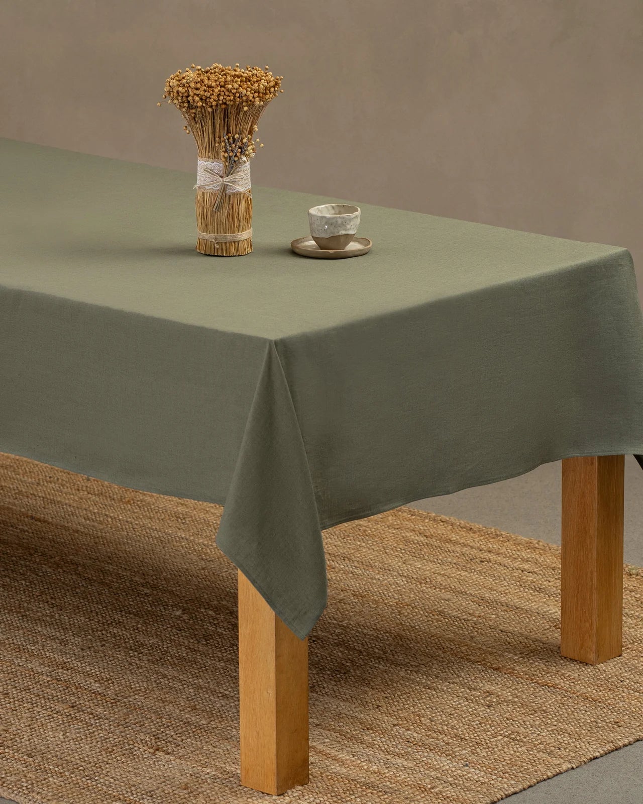 Stone green tablecloth on a wooden table with a small decorative arrangement and cup.