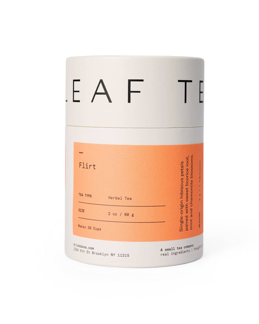 A cylindrical package labeled 'Flirt Tea' with text indicating the herbal tea consists of dried leaves namely a blend of hibiscus petals paired with sweet licorice root, mint and chamomile blossoms. It has a distinctive orange and white label design.
