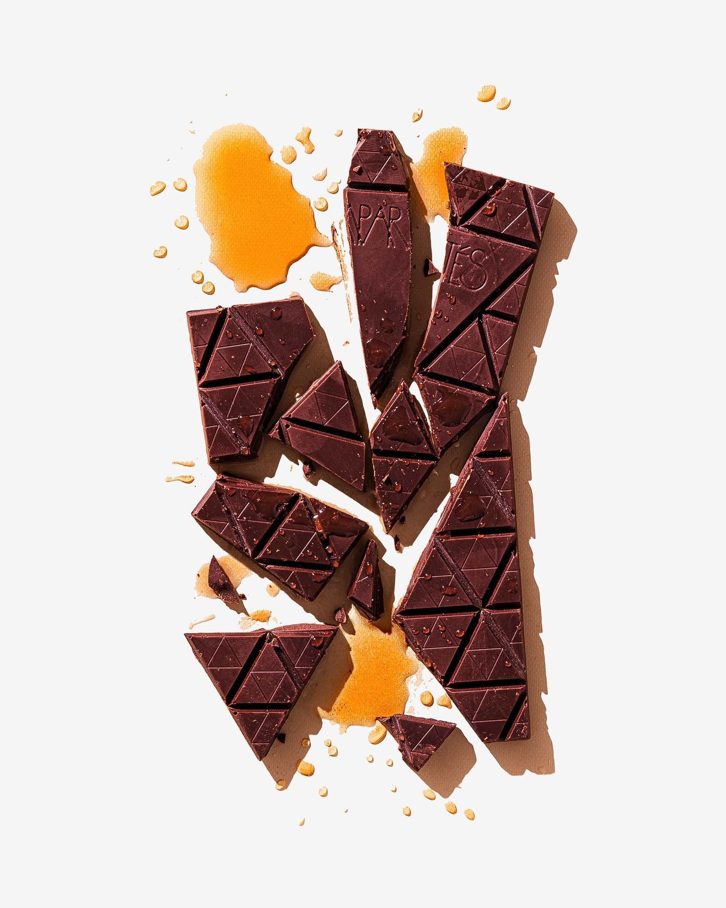 Dark chocolate bar broken in chunks with a splash of whisky on a white background