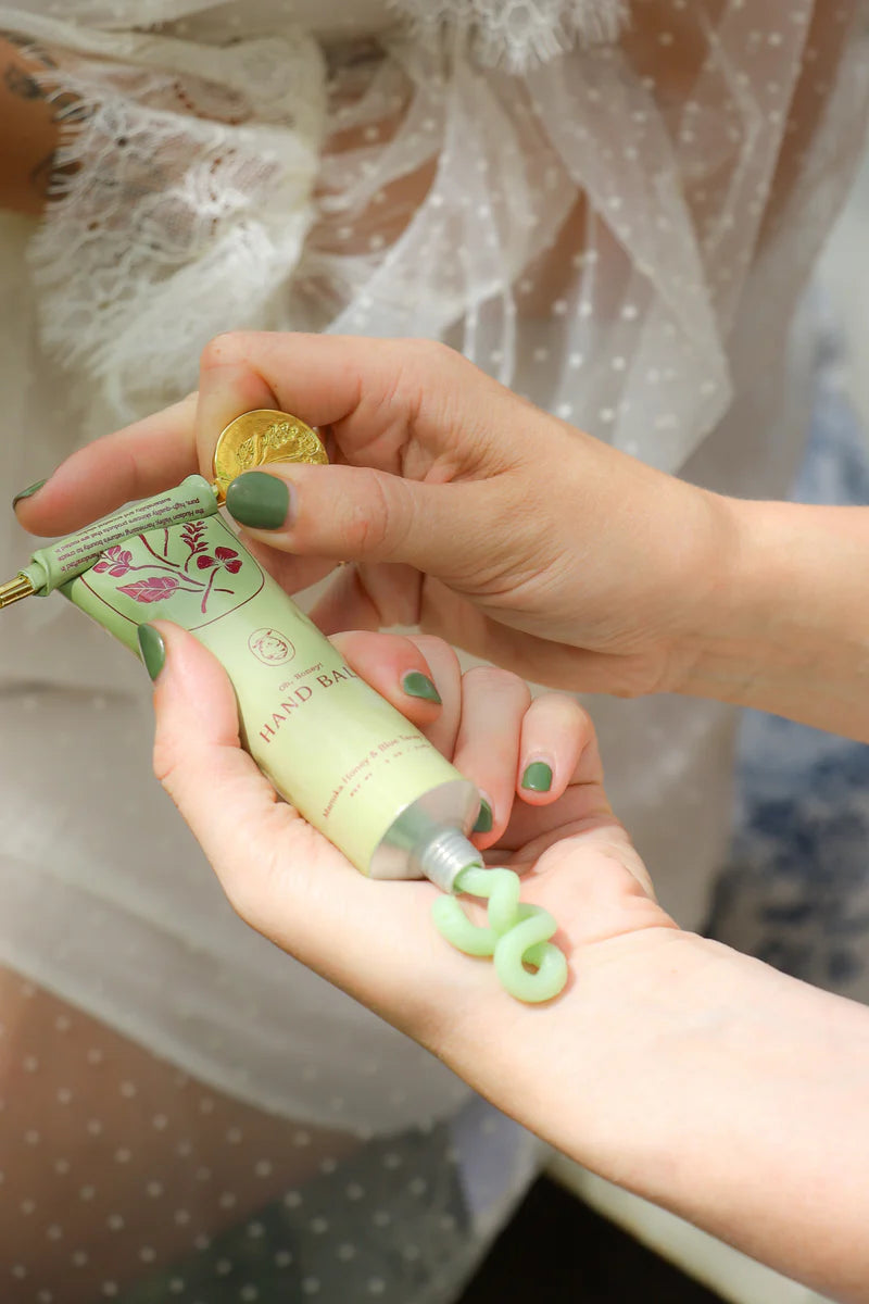 Hand holding a green hand balm from my neighbor's tallow with a blurred background