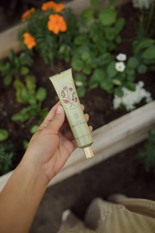 Hand holding a green tube of hand cream with a garden in the background