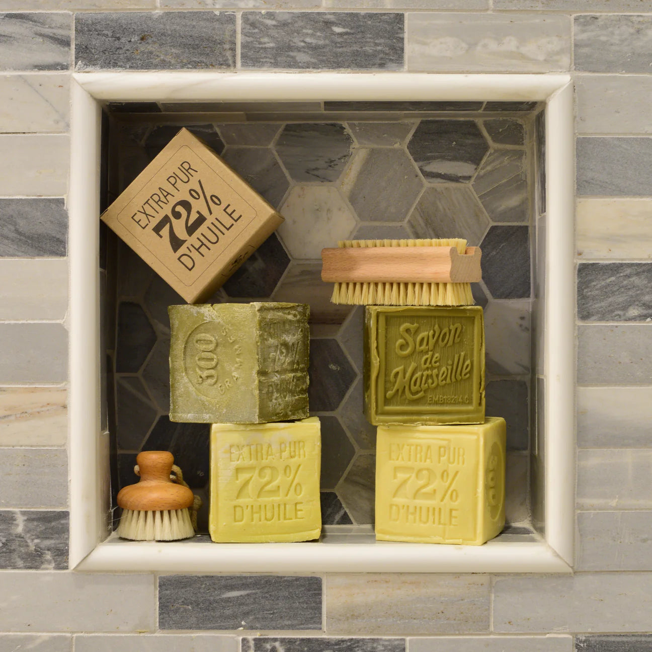 Set of Marseille soap bars and brushes in a shower caddy with tiled background