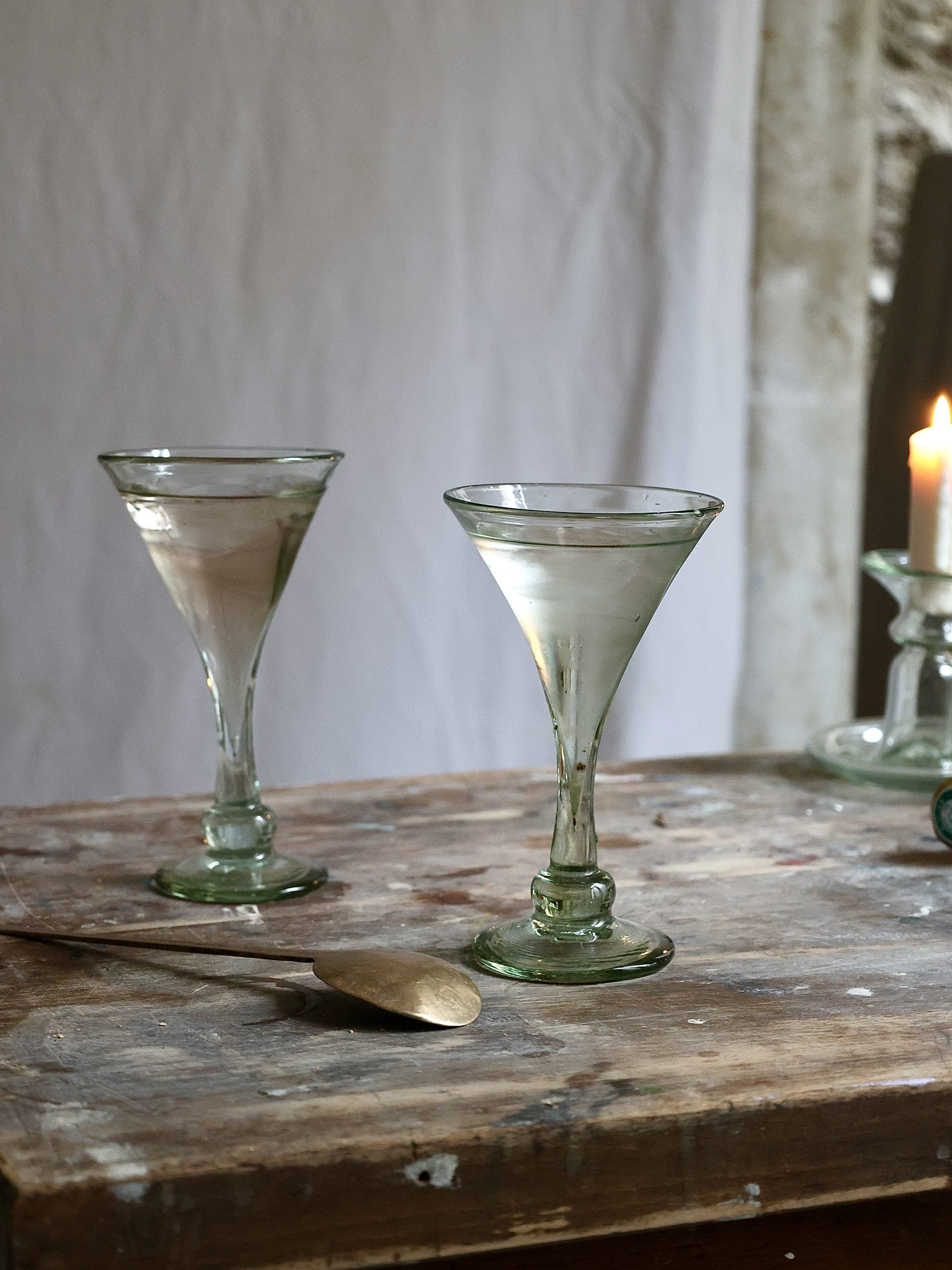 Two vintage-style martini cocktail glasses on a rustic wooden table with a candle in the background.