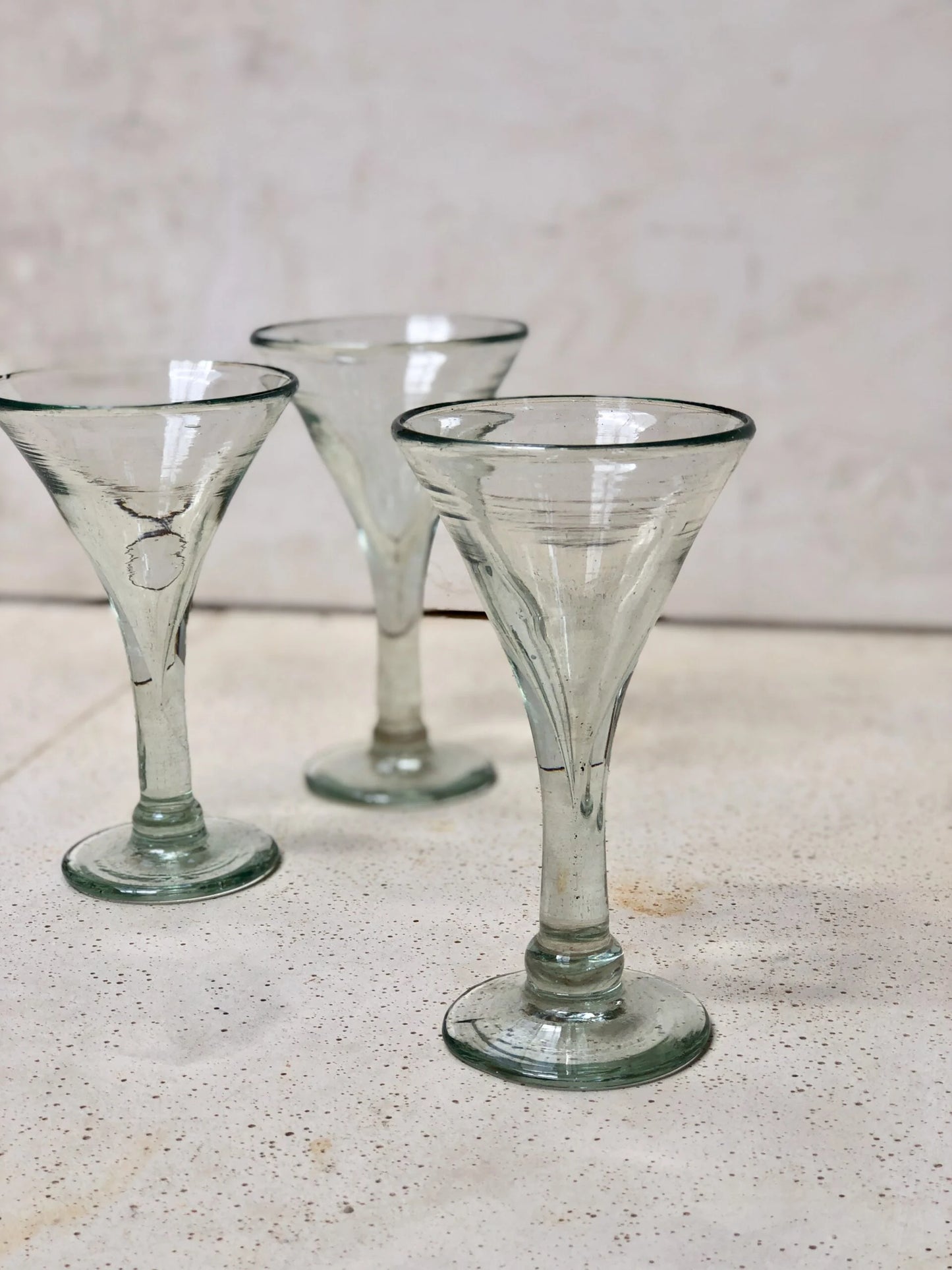 Three elegant vintage-style clear glass cocktail glasses on a light surface with a neutral background. Details are proof that the glasses are mouth-blown.