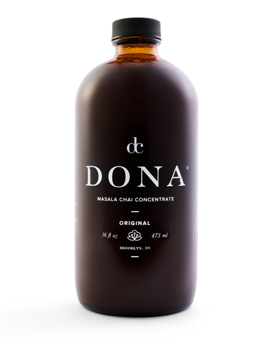 A 16oz glass bottle of Dona Masala Chai Concentrate with a black cap and label that includes the brand name and the product name. The bottle is marked as original and is positioned against a white background.