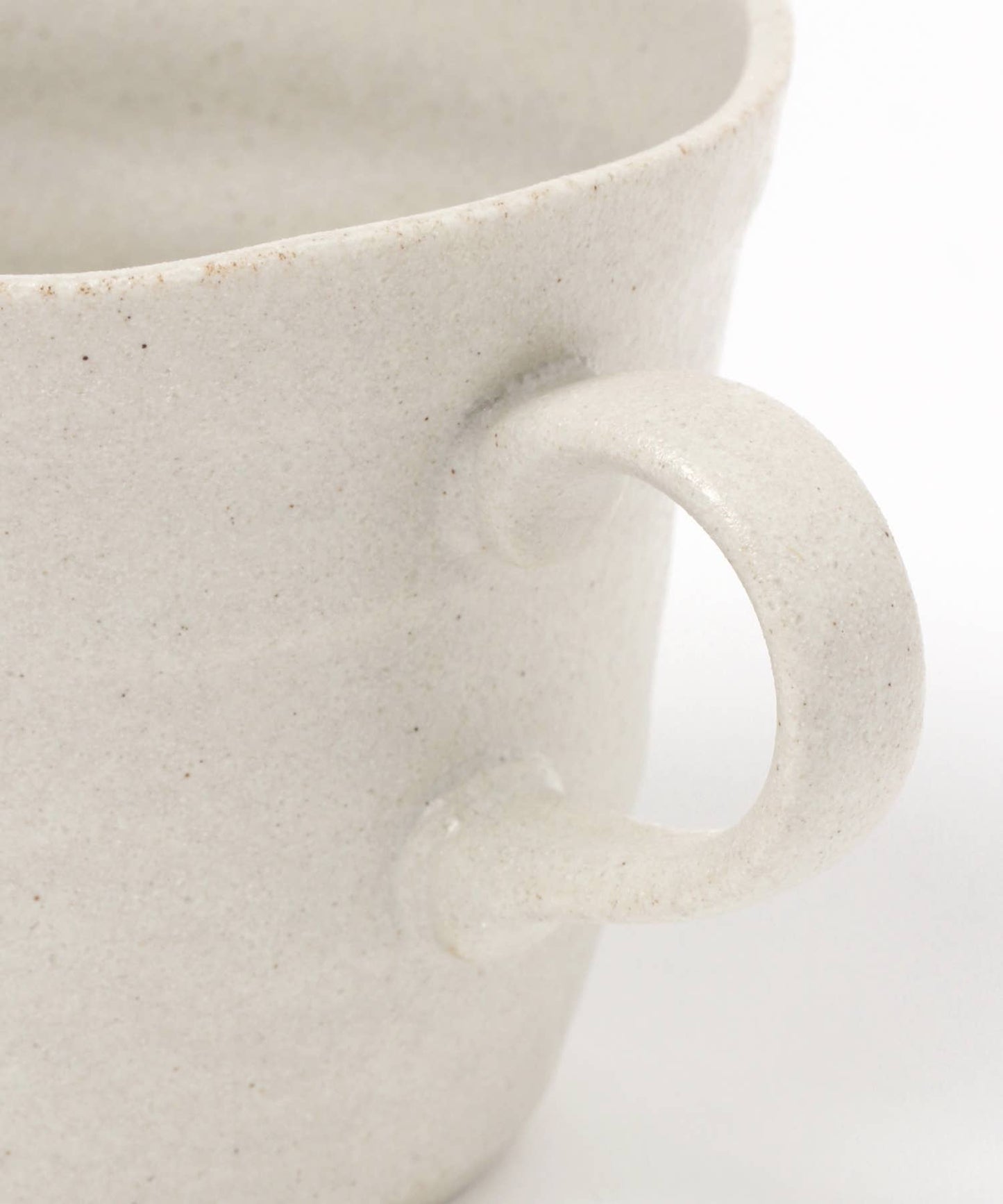 Close-up on the handle of a white ceramic mino ware mug with an organic shape on a white background.