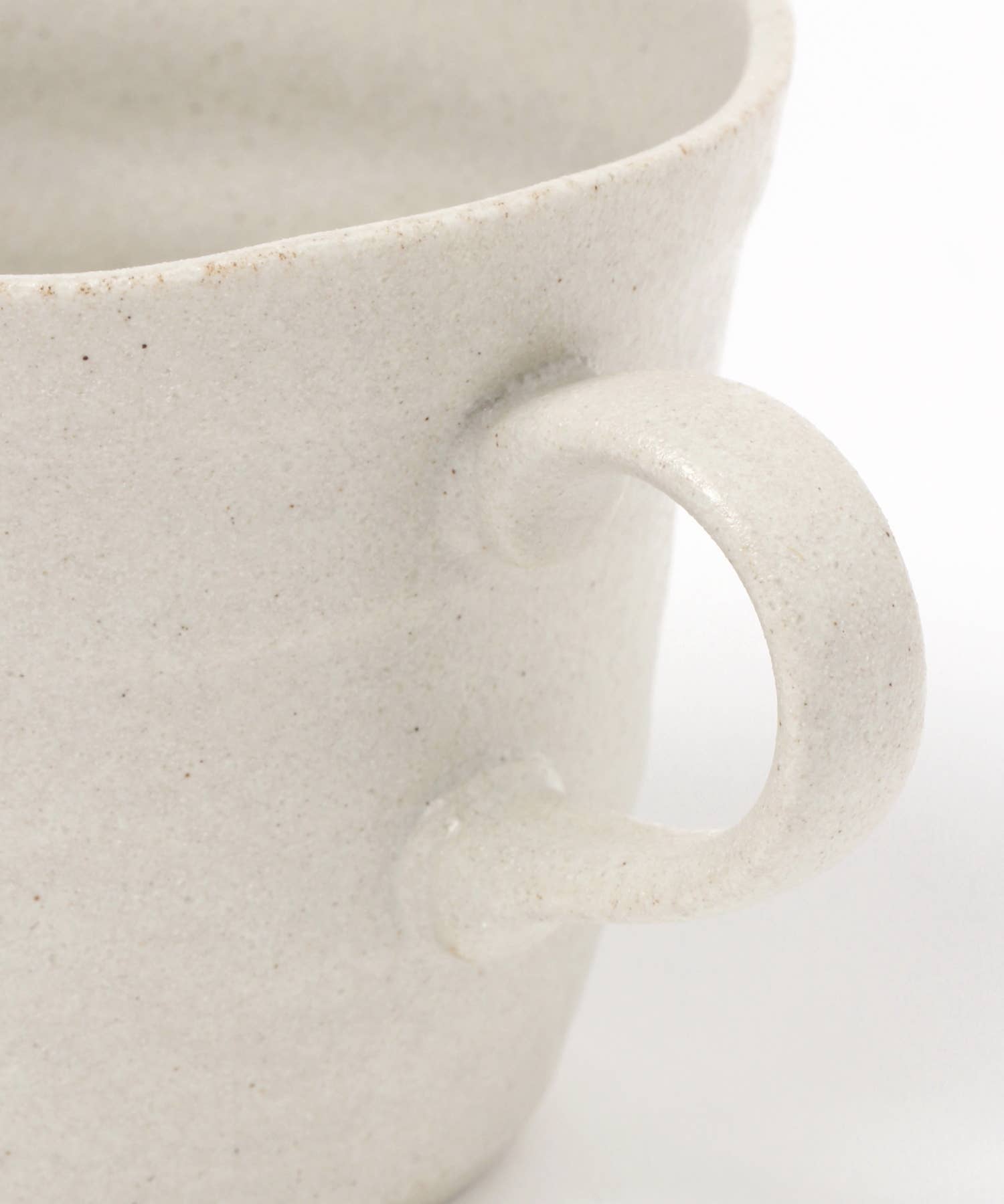 Close-up on the handle of a white ceramic mino ware mug with an organic shape on a white background.
