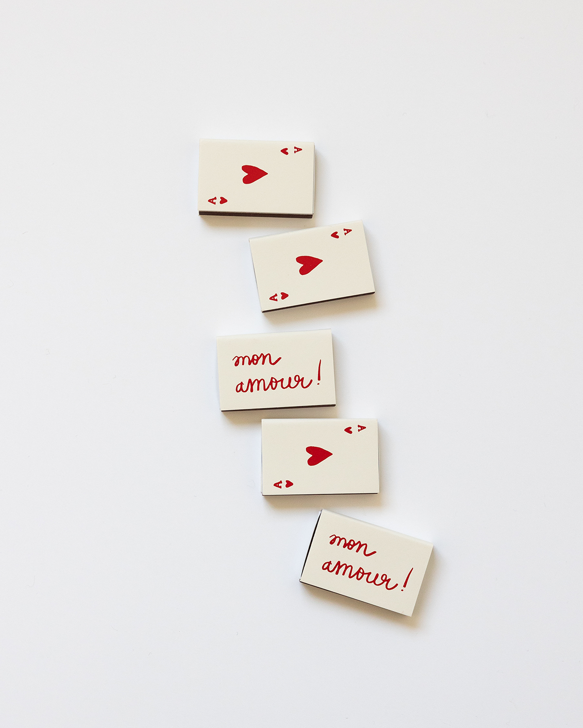 A beige-colored matchbox with the text 'Mon Amour' and a heart symbol printed in a red color on the front, symbolizing  an ace of hearts card.
