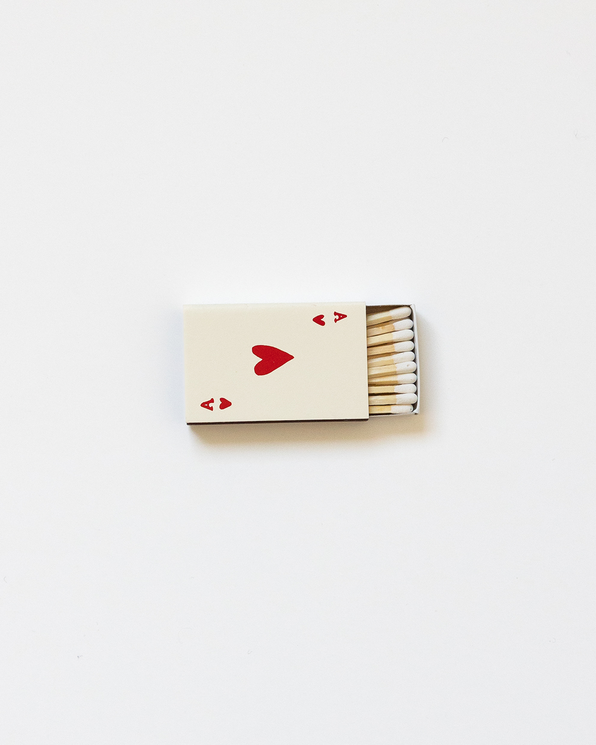 A beige-colored matchbox with a heart symbol printed in a red color on the front, symbolizing an ace of hearts card.