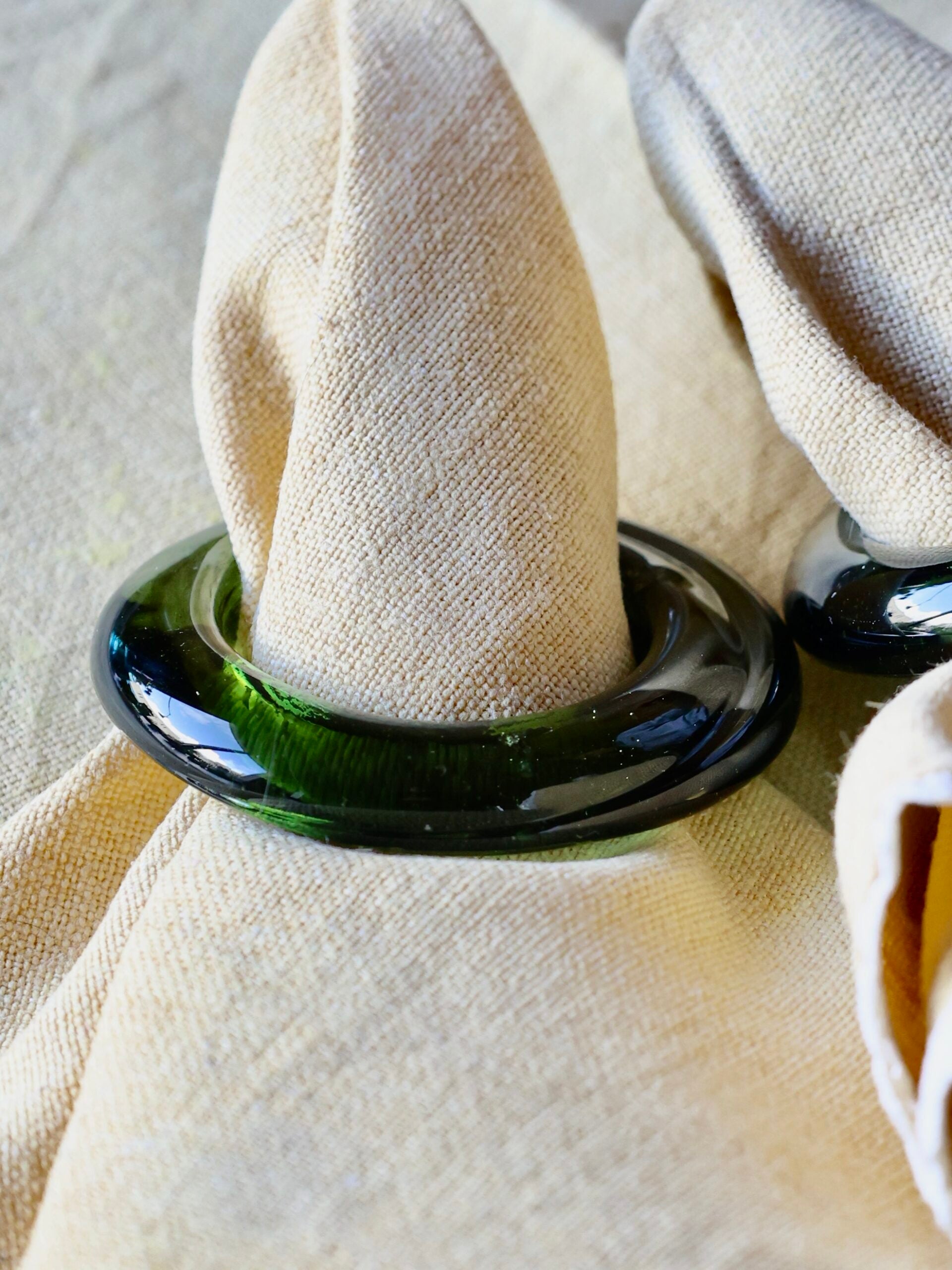 Napkin ring in smoked green glass holding a white napkin on a textured surface