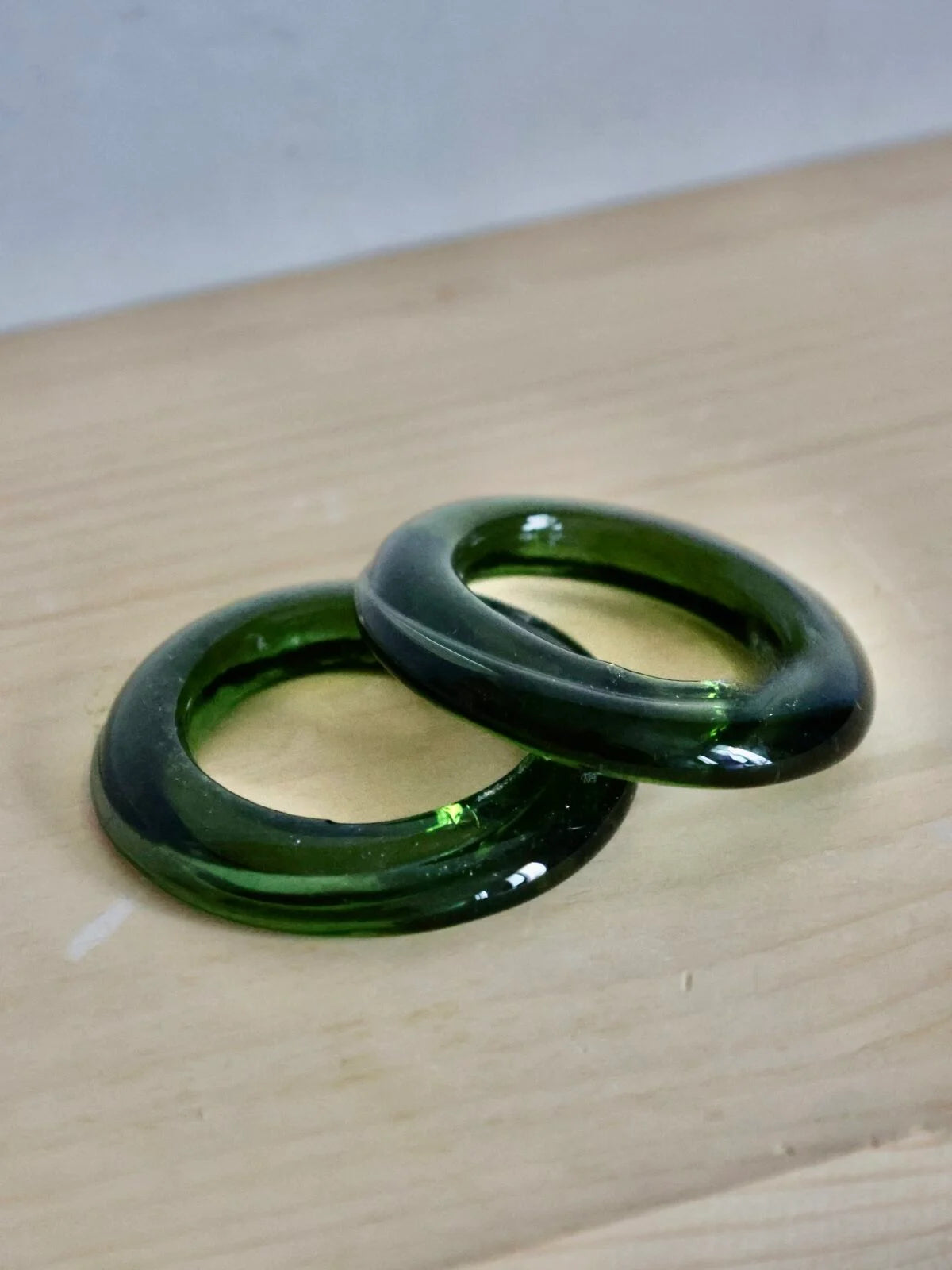 Two artisanal green glass rings on a wooden surface