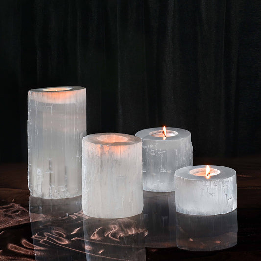 A set of four clear selenite crystal tea light holders on a reflective surface with a dark background.