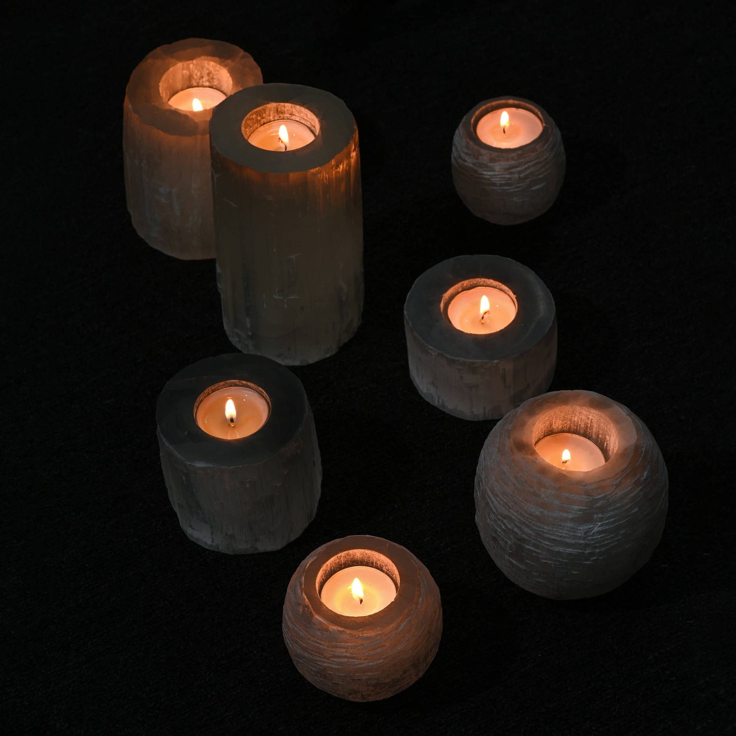 Set of seven crystal candles holders glowing with warm light on a dark background.