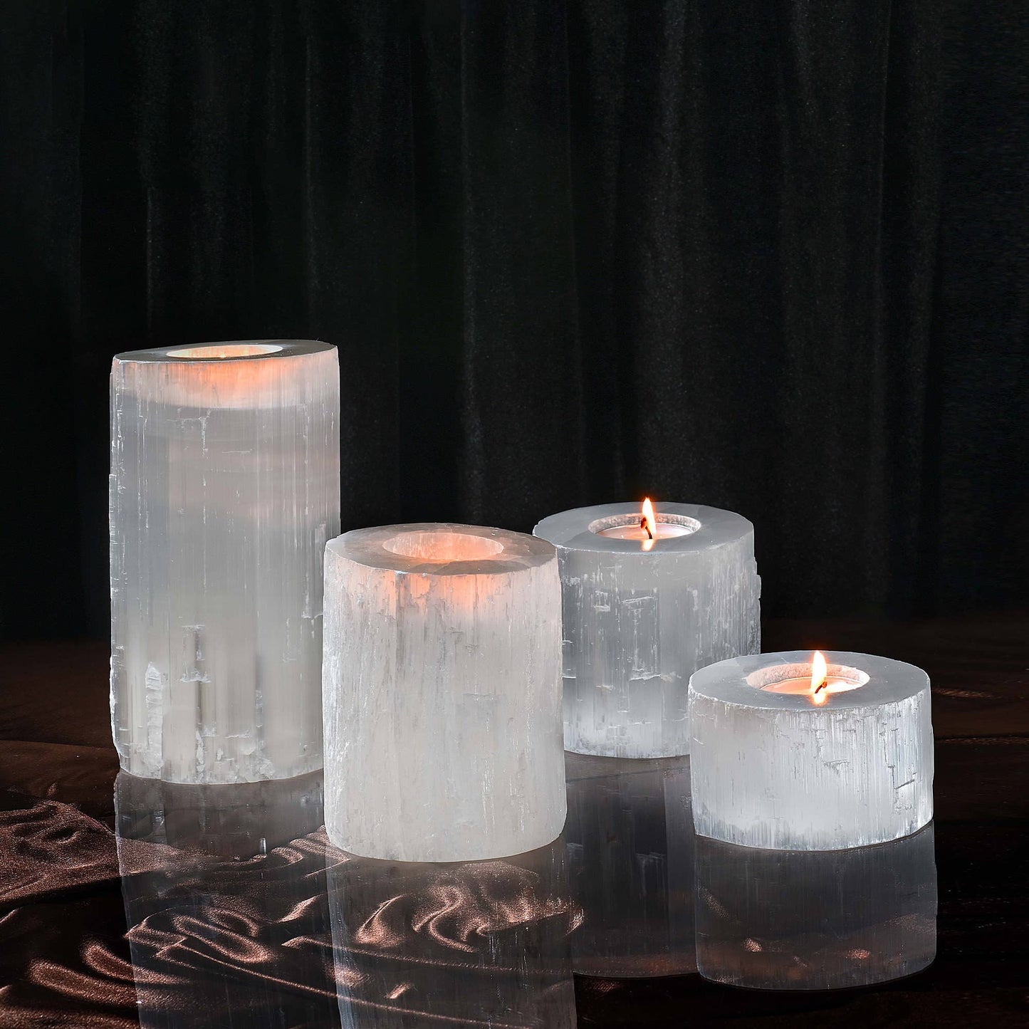 A set of four clear selenite crystal tea light holders on a reflective surface with a dark background.