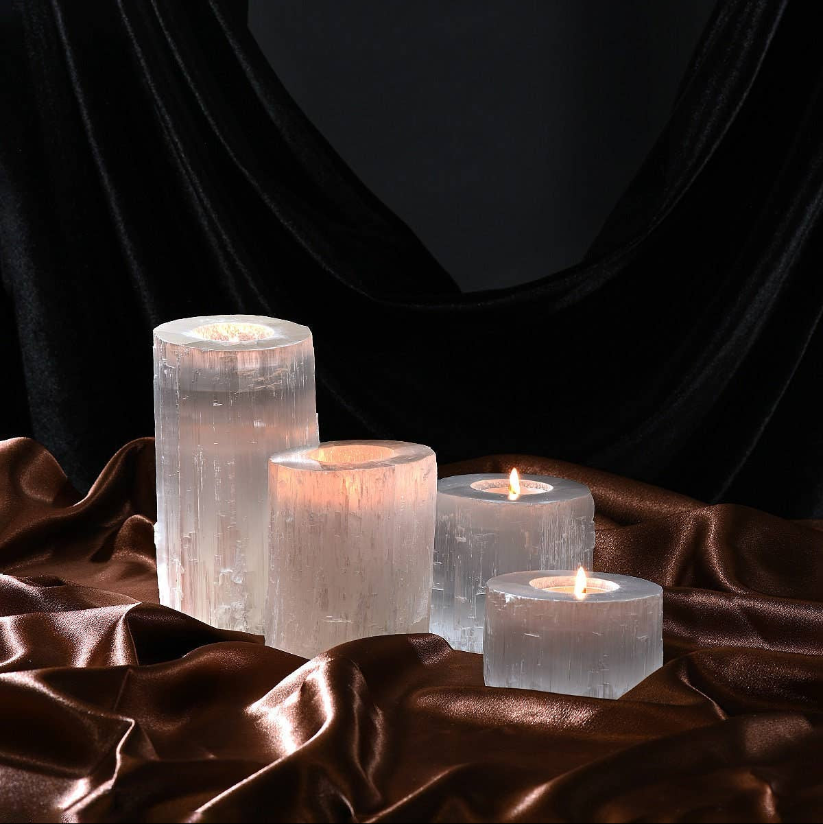 Set of four crystal candles holders glowing with warm light on a dark fabric background