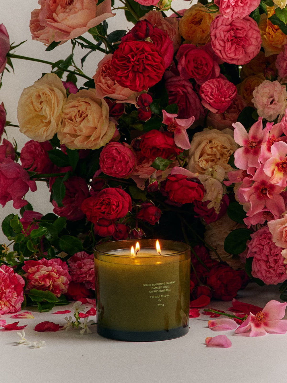 Candle with flames in front of a vibrant floral arrangement