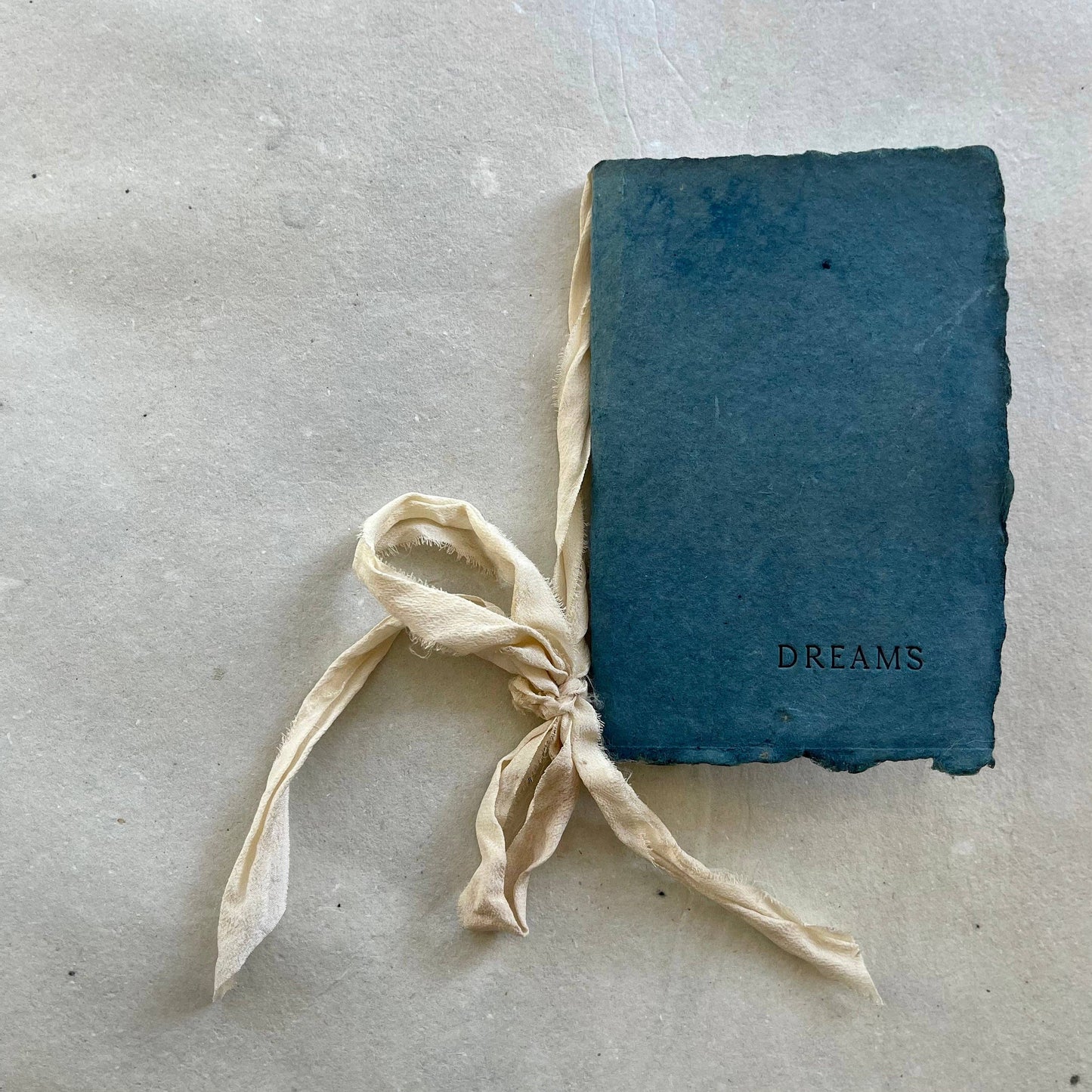 A handmade notebook with a soft cloud ribbon and botanical-dyed cover in indigo color, labeled "DREAMS".