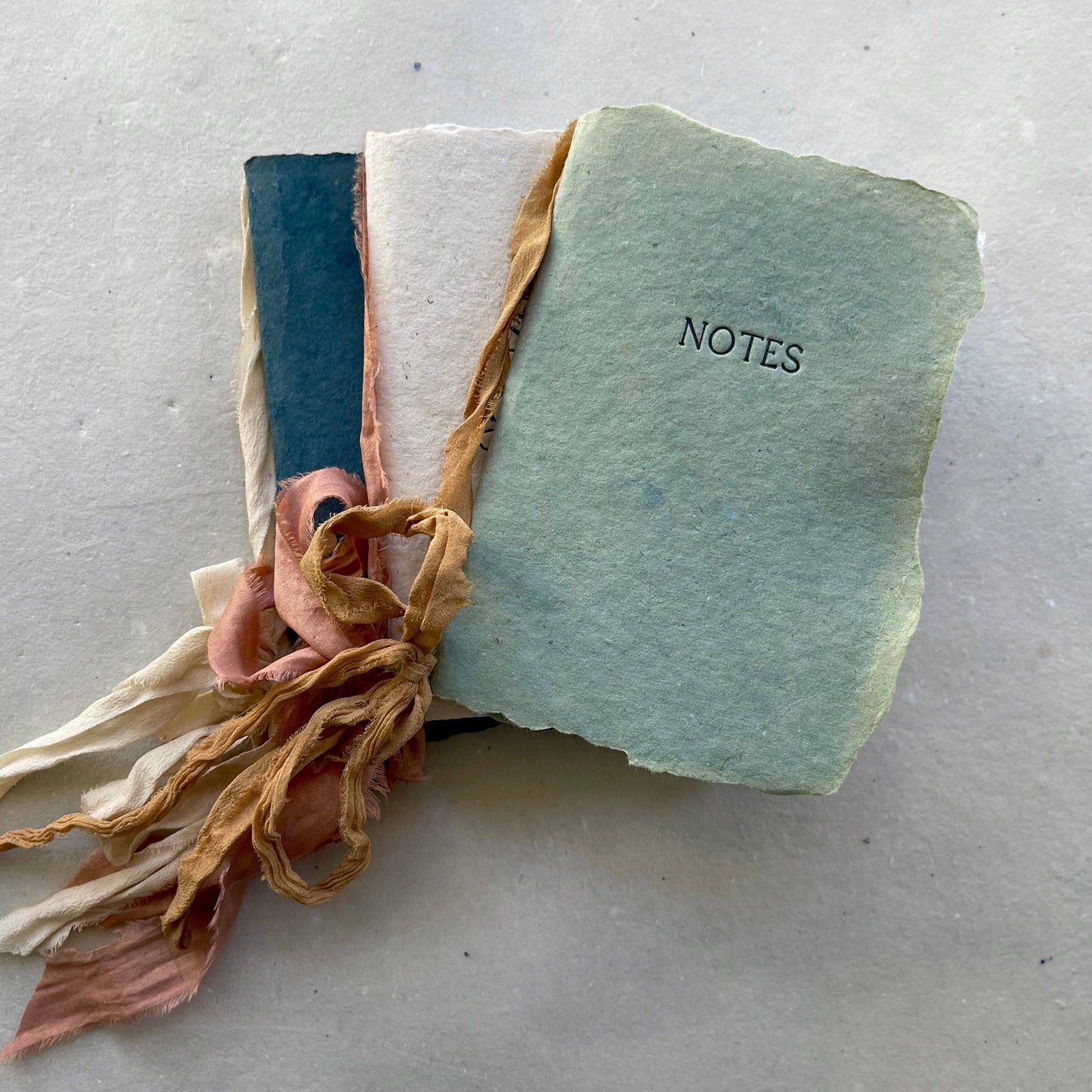 A handmade notebook with a camel ribbon and botanical-dyed cover in oak green color, labeled "NOTES".