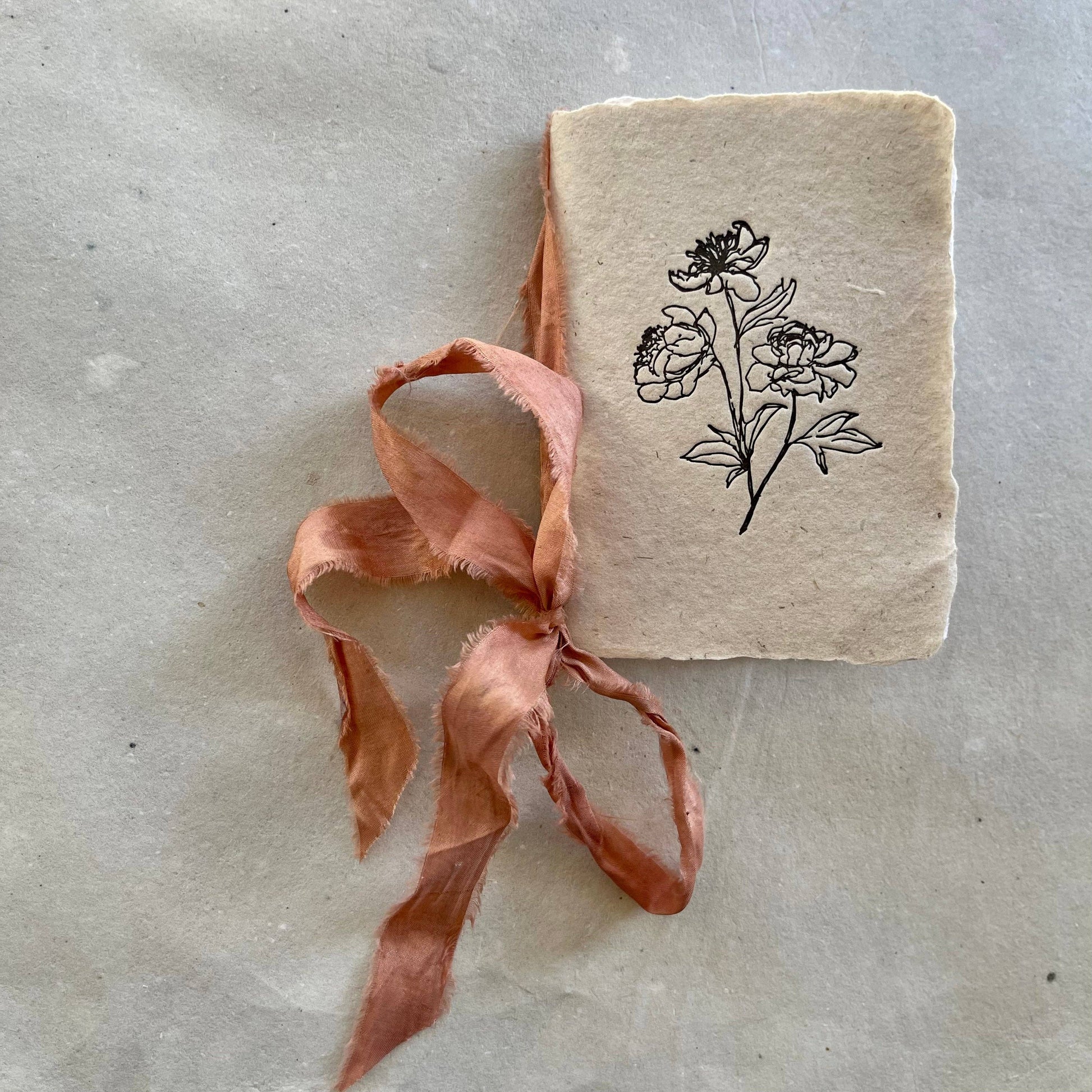 A handmade notebook with a watermelon silk ribbon and botanical-dyed cover in vanilla color.