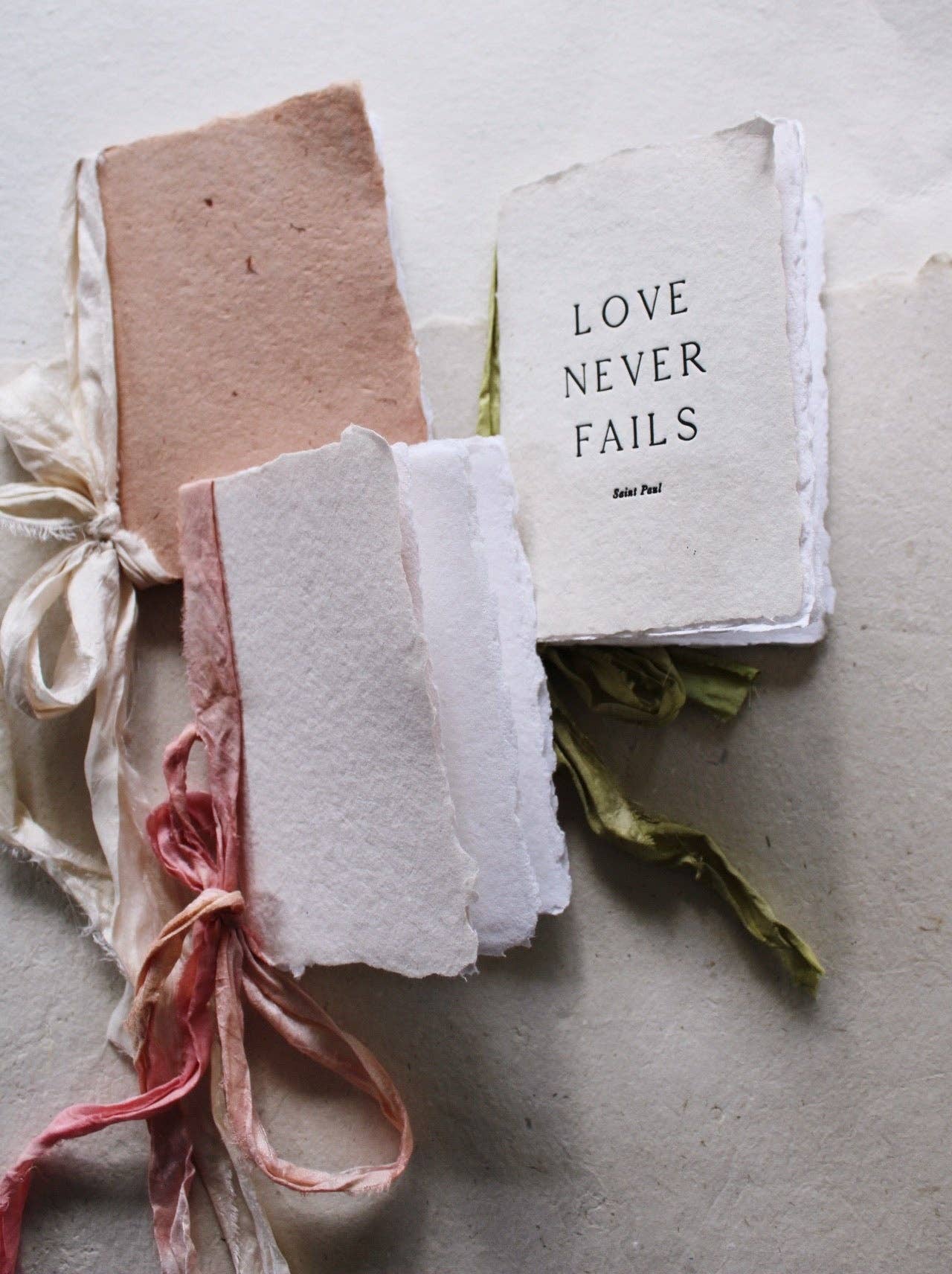A collection of notebooks with various types of handmade paper covers in beige, pink, and white, tied with silk ribbons.