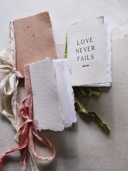 A collection of notebooks with various types of handmade paper covers in beige, pink, and white, tied with silk ribbons.