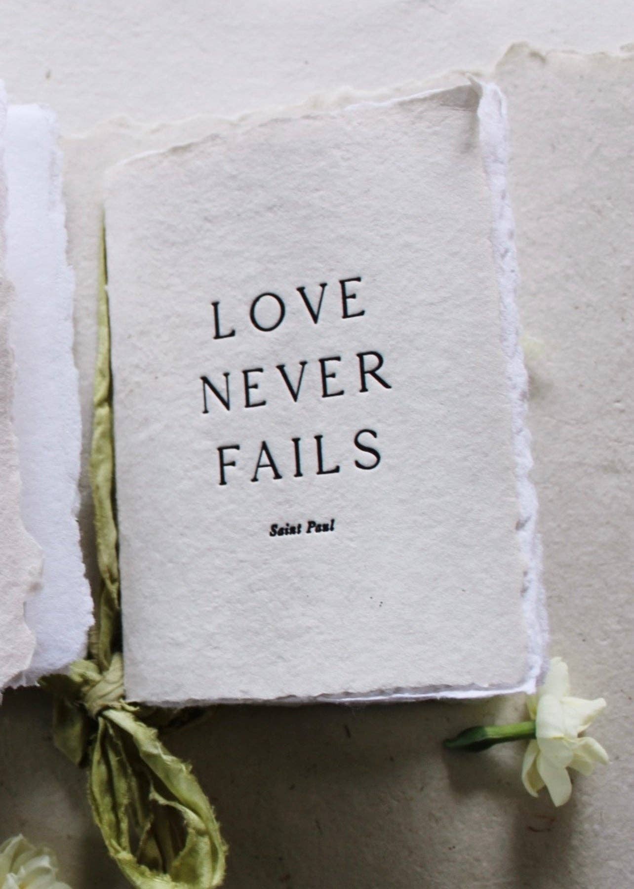 A handmade vanilla notebook with a pear green silk ribbon and botanical-dyed cover, labeled 'Love never fails'.