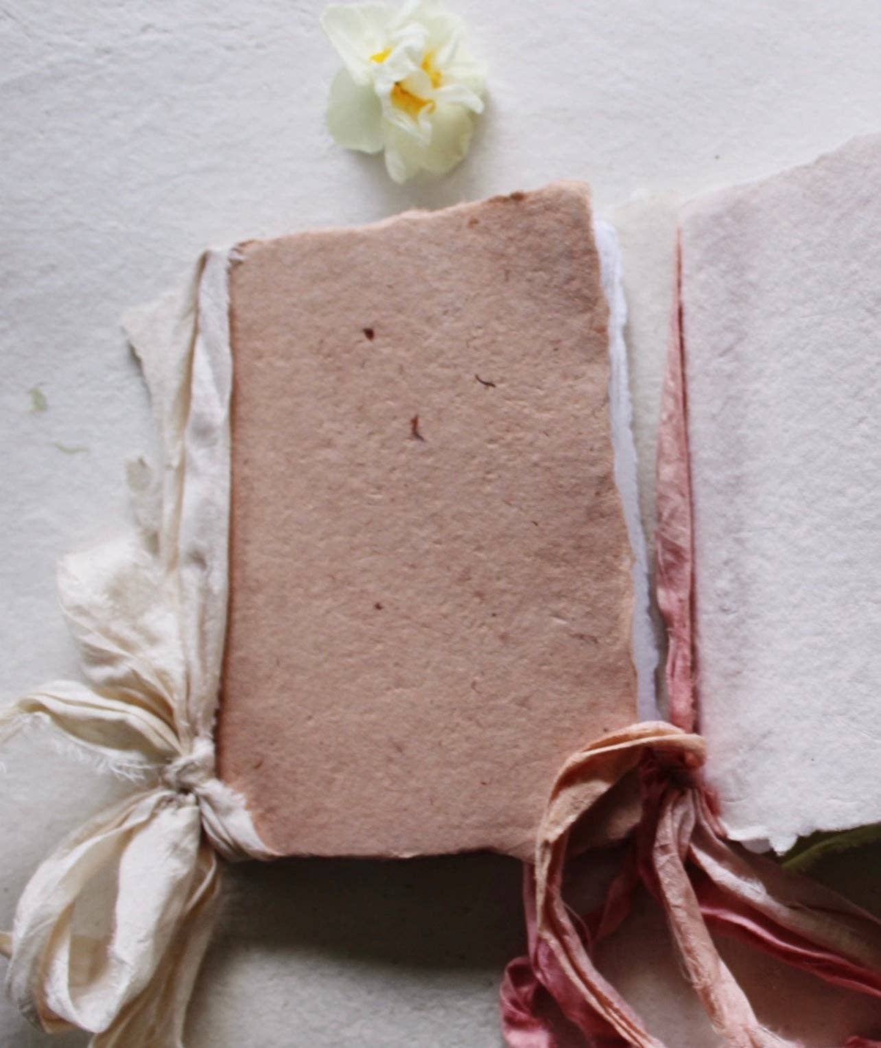 A handmade notebook with a soft cloud silk ribbon and botanical-dyed cover in rose color.
