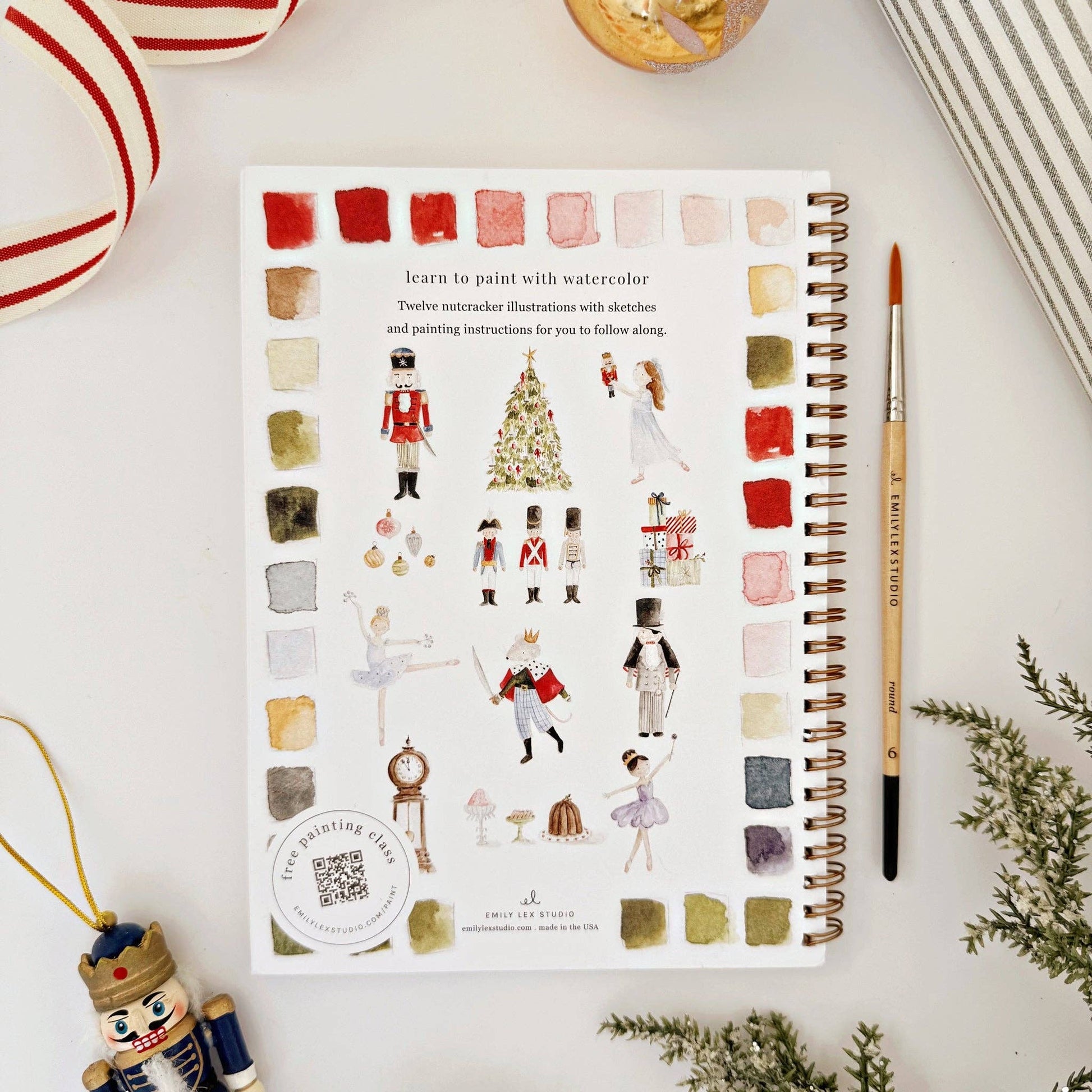 Creative mindfulness workbook with watercolor illustrations and paint swatches on a white surface with Christmas decorative items.