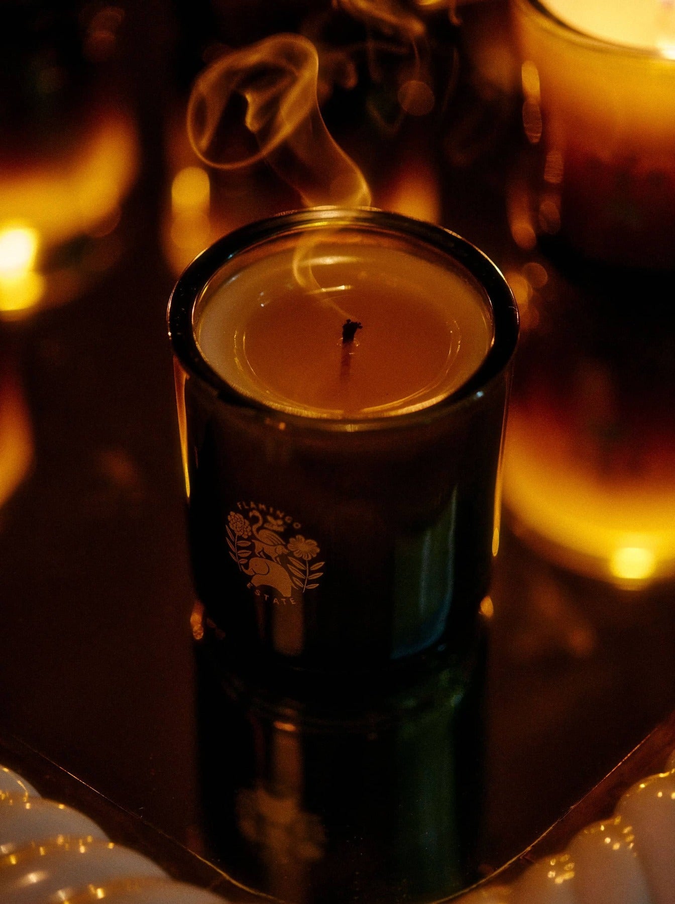 Candle in a dark container with a blurred candle in the background