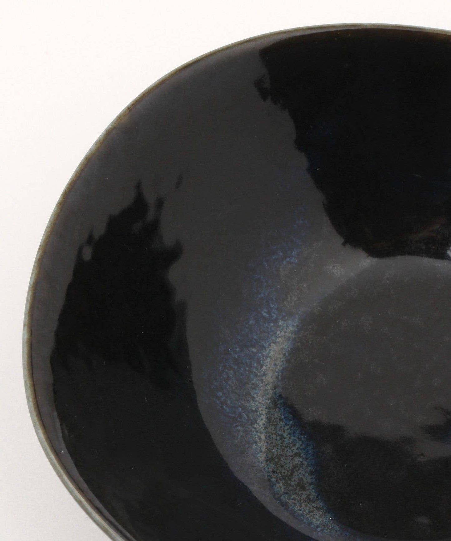 Close-up on a gloss black ceramic mino ware mini bowl with an organic shape on a white background.