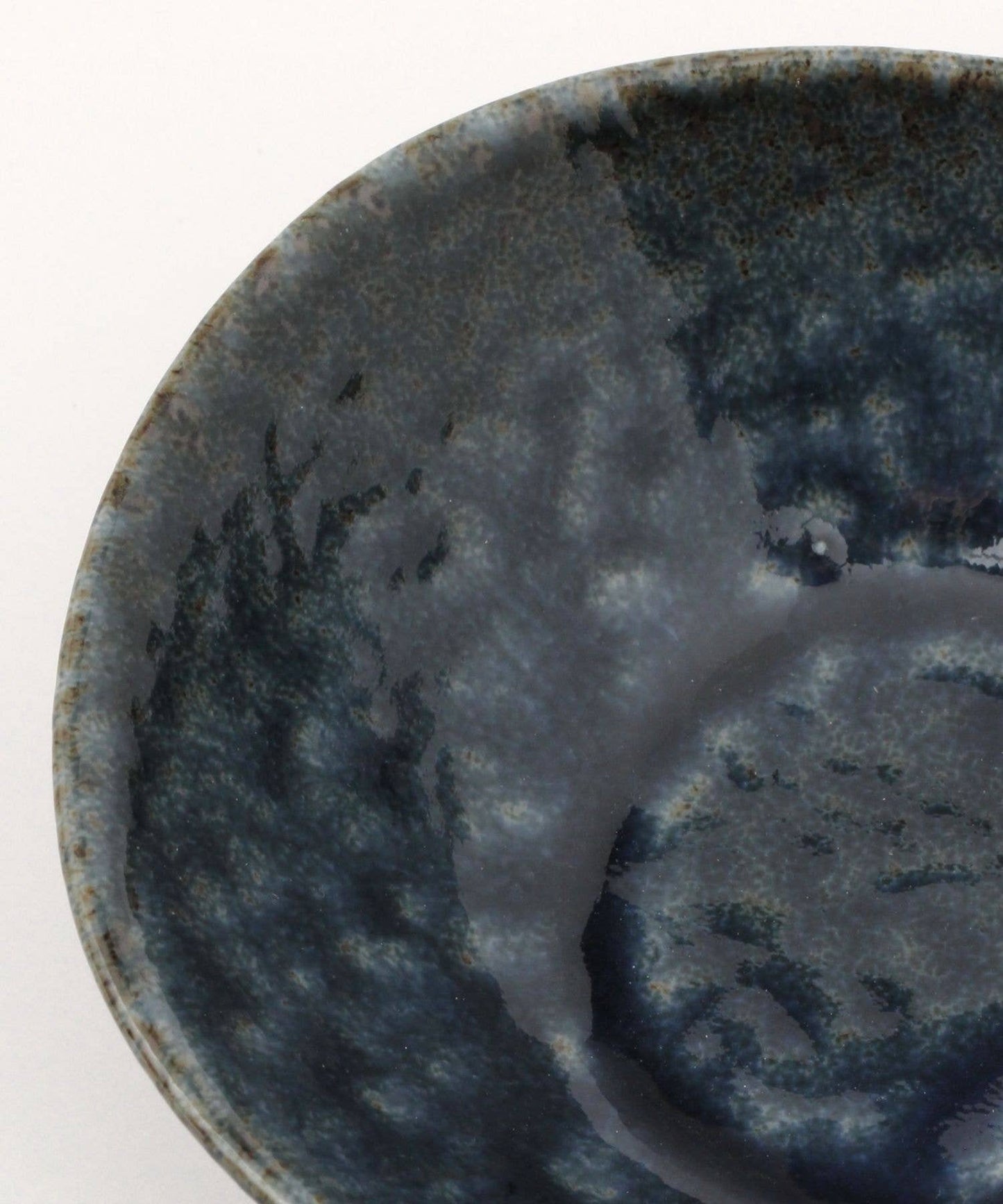 Close-up on a dark blue ceramic mino ware mini bowl with an organic shape on a white background.