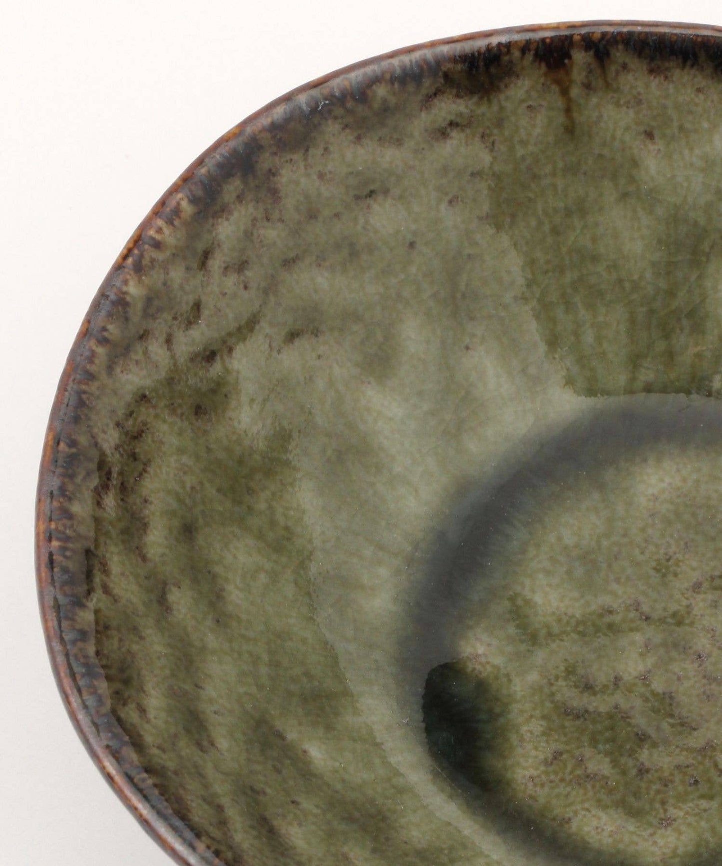 Close-up on a moss green ceramic mino ware mini bowl with an organic shape on a white background.