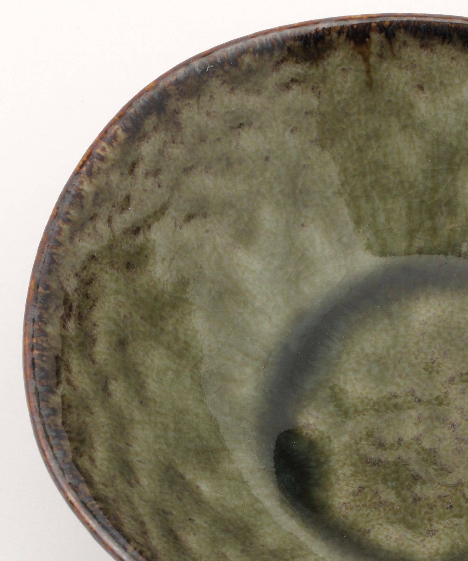 Close-up on a moss green ceramic mino ware mini bowl with an organic shape on a white background.