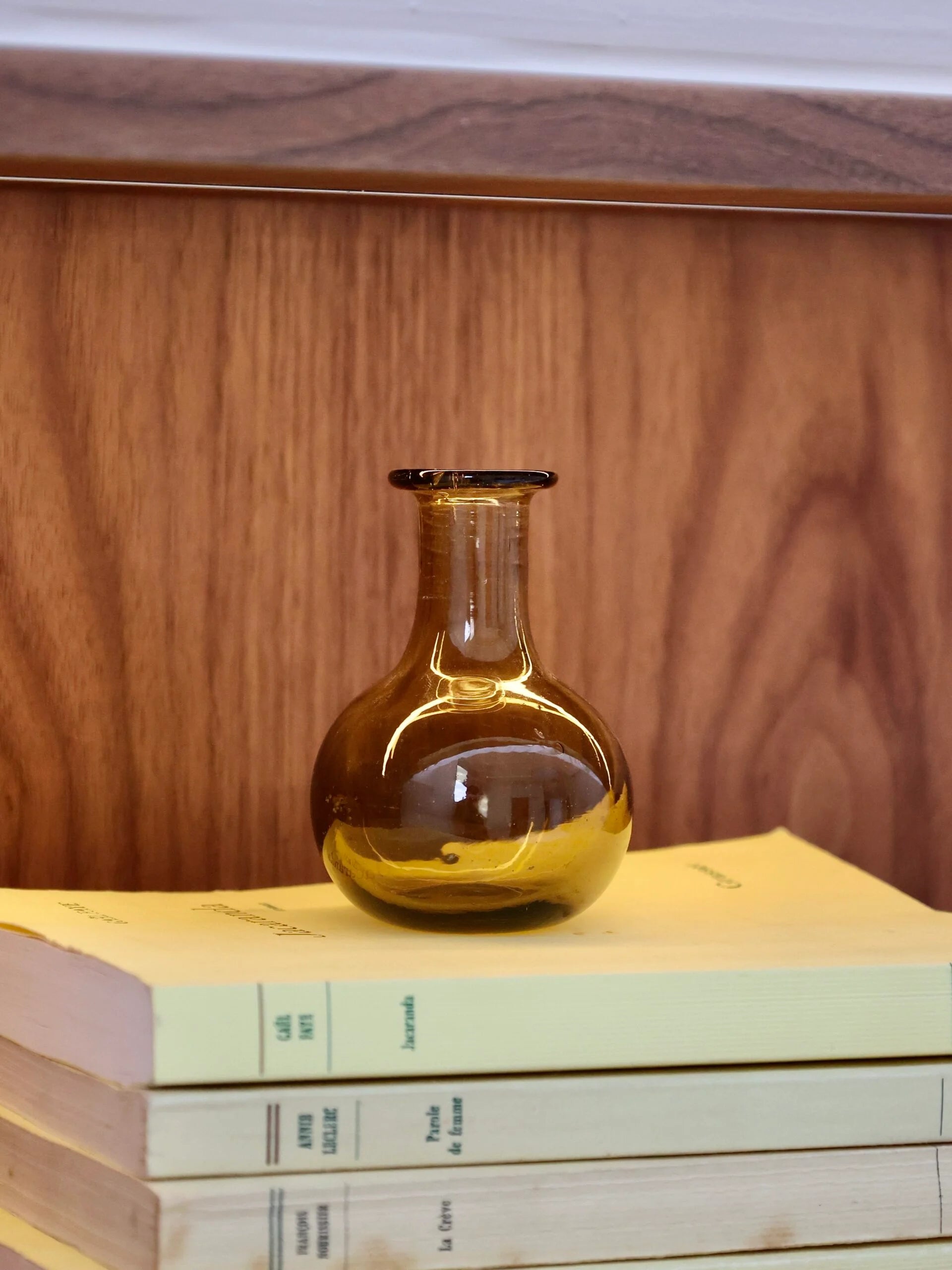 Amber glass bottle that can serve as a vase on a stack of books against a wooden shelf background