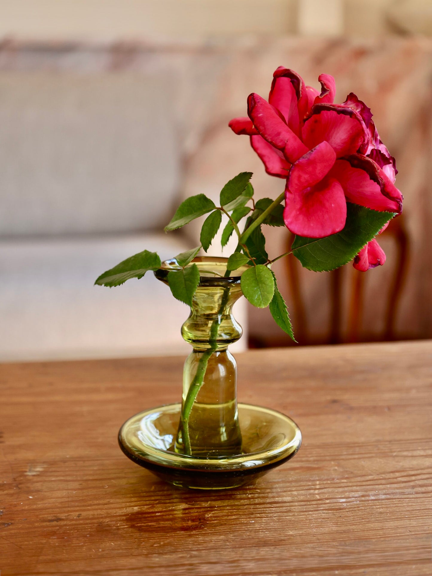 Pink rose in a small handmade glass vase on a wooden surface with a blurred background