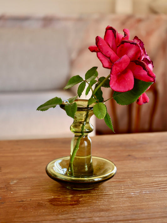 Pink rose in a small handmade glass vase on a wooden surface with a blurred background